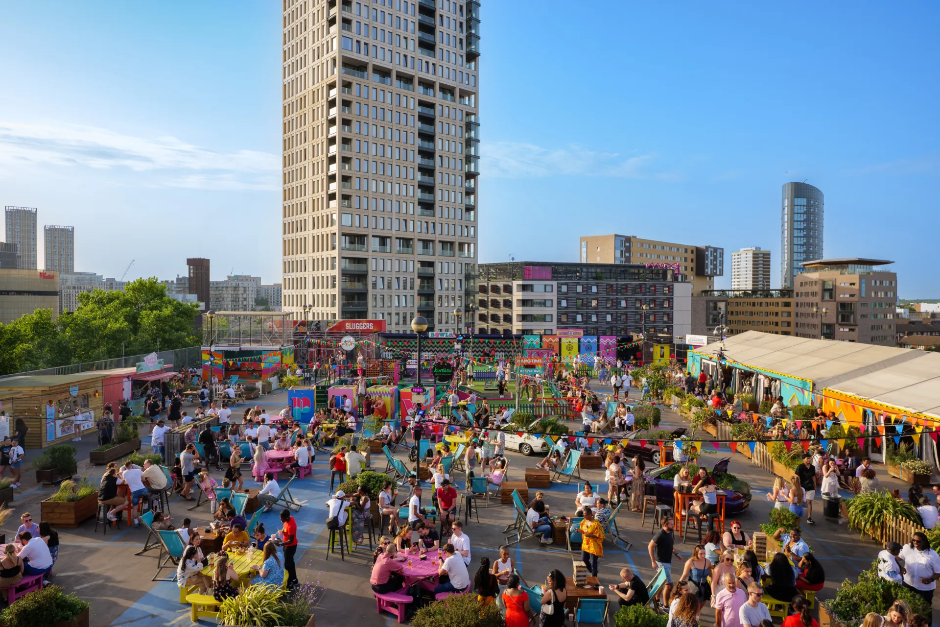 Photo of a crowded rooftop bar with tall buildings in the background